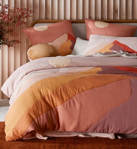 a front view of a bed with Maus Haus bedspread and cushions.