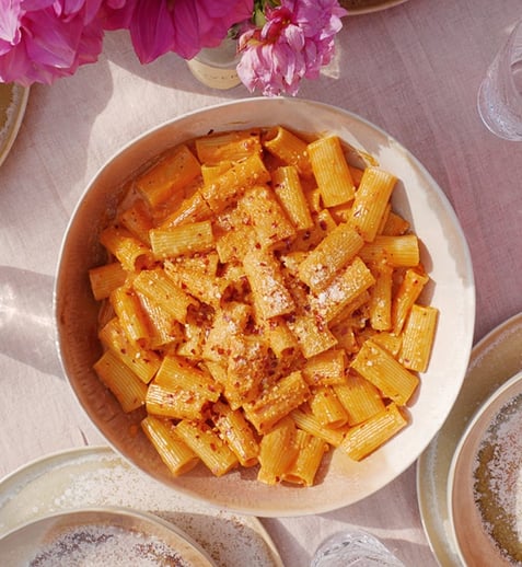 An aerial shot of a bowl of pasta alla vodka on a table surrounded by serving ware and clear drinking glasses.