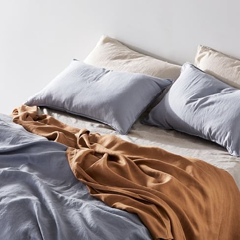 Close-up of bed made with Vintage Washed Linen Bedlinen – including blue, caramel, and linen colours. 
