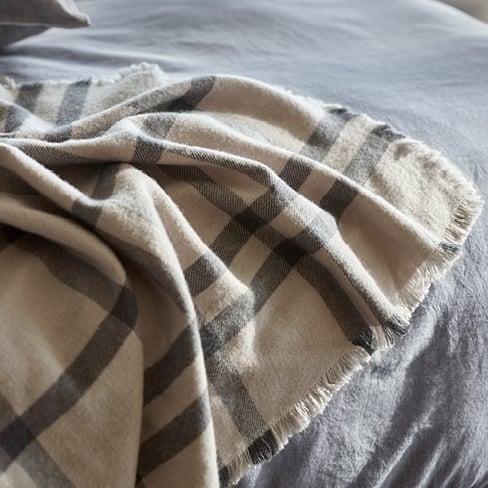 Bed with a close-up of Mark Tuckey Throw – with a classic check design in grey and navy made from Australian lambswool.
