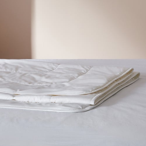 Cotton quilt folded placed on top of a bed.