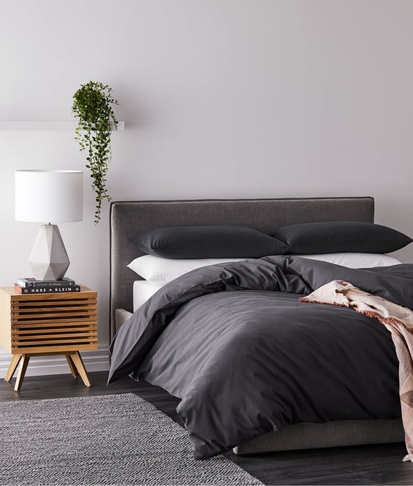 Bed styled with black bedlinen, white sheets, side table and lamp - quilt sits low, bottom edge touching the floor. 