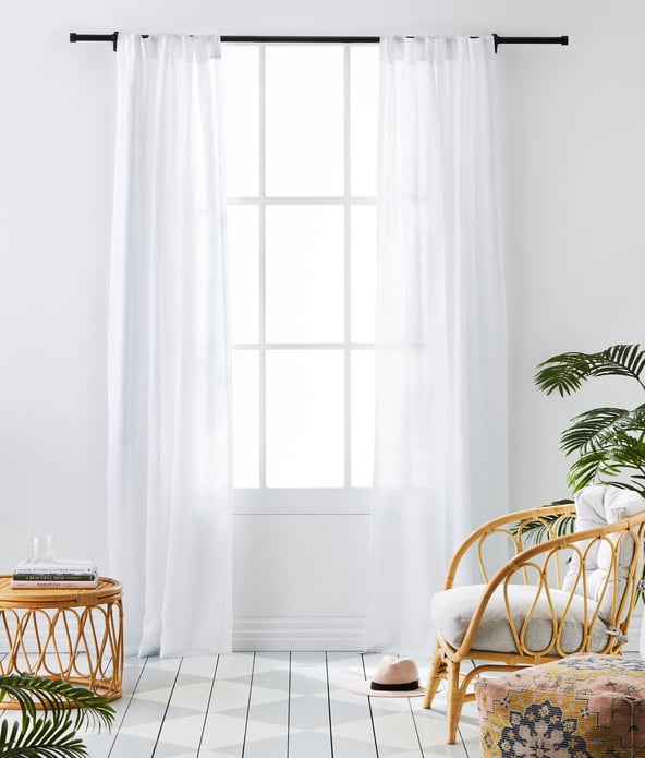 Living space scene of a window with white linen curtains displayed behind a bamboo coffee table and chair