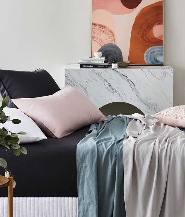Bed displayed with bamboo linen set, bed sheets in black, quilt covers in shades of blue and grey and black white and pink pillows