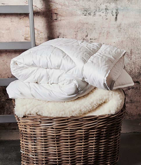 White minijumbuk wool mattress topper folded and placed onto a dark brown bamboo basket