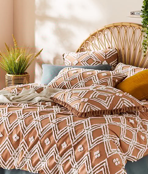 Terracotta bedlinen with textured tufting in diamond patterns on a bed with a rattan bedhead and colourful accessories. 