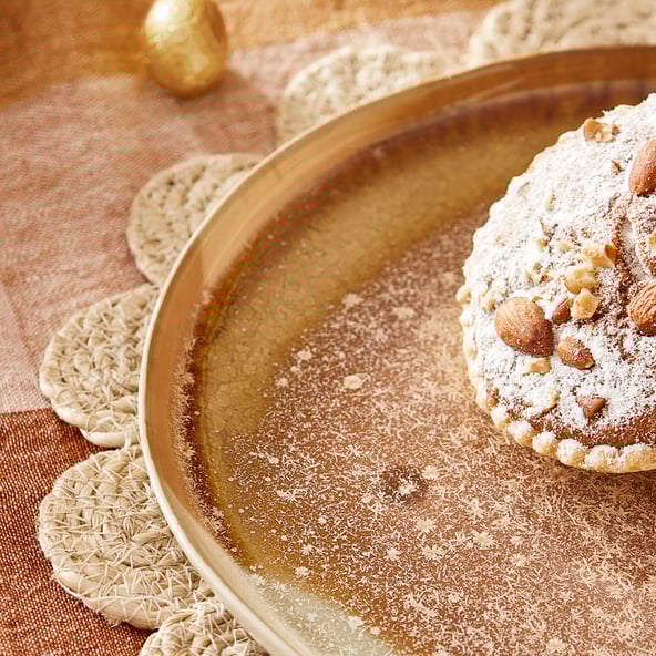 A close up, cropped image of a tart set on a brown plate, with a woven placemat underneath. The tablecloth is gingham and there are two Easter eggs towards the top of the frame.