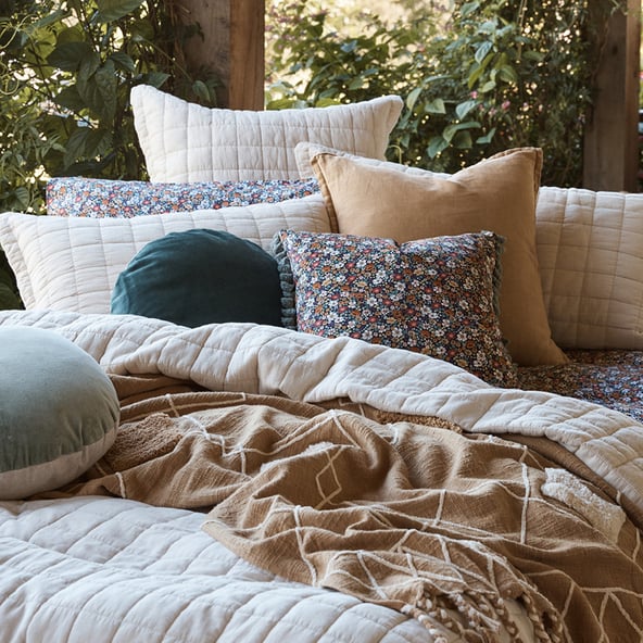 A close up, angled view of floral, velvet and quilted cushions arranged on a bed