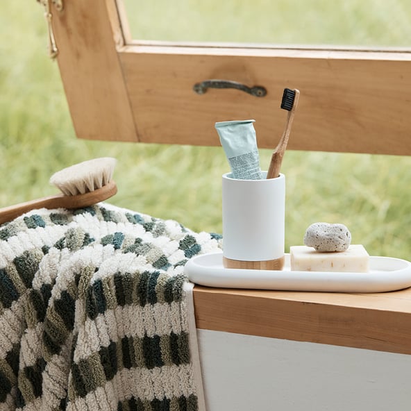 A green patterned towel and a small marble tray filled bathroom accessories sits on a window sill in front of the slightly ajar window.
