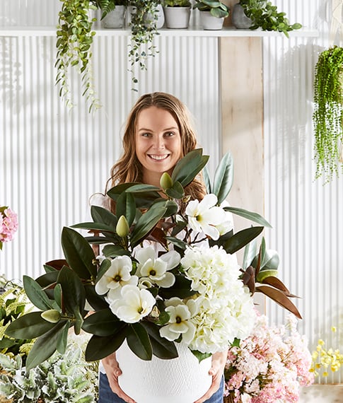 Woman in smiling holding a large selection of statement flowers and leaves.