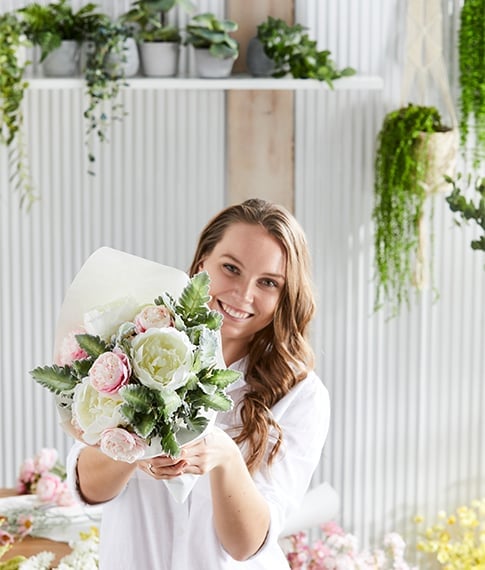 Woman smiles while holding a beautifully curated bunch of posies, in the light shades of pink and white.