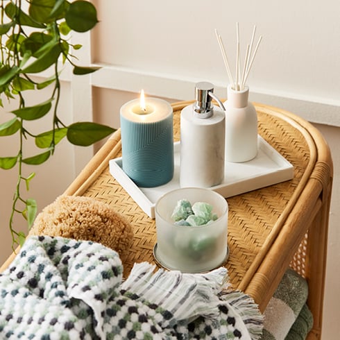 Close-up of rattan table with towels on the shelf, on top sits a towel and marble tray with bathroom essentials.