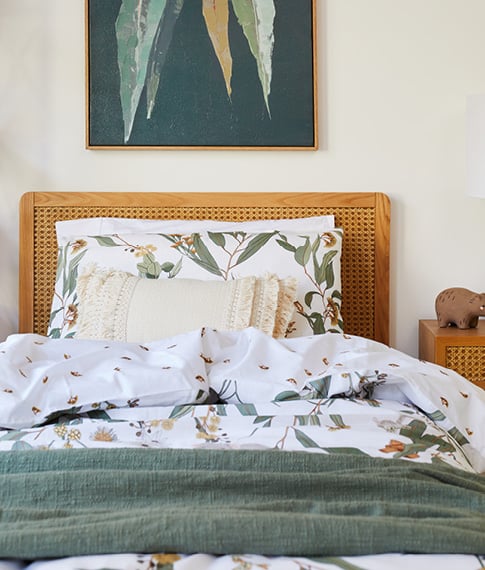 Close-up of kids’ bed with botanical bedlinen, linen green throw, tufted cushion, and Arden Rattan Bed and Side Table.