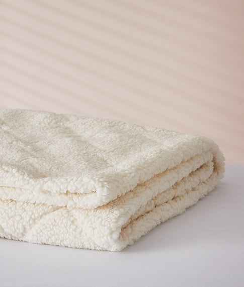 Soft Wool Mattress Topper folded and stacked on top of a white bed. 