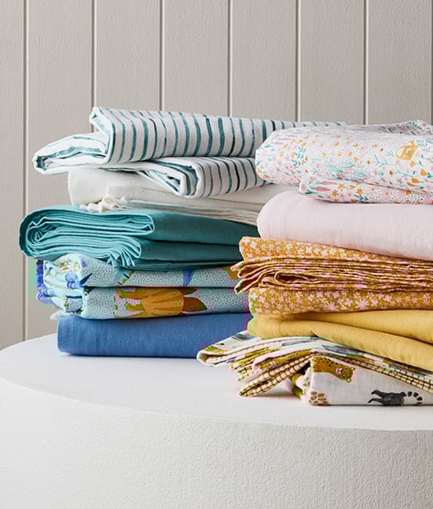 Two stacks including printed, plain and patterned kids flannelette sheets sitting next to each other on a white round table. 