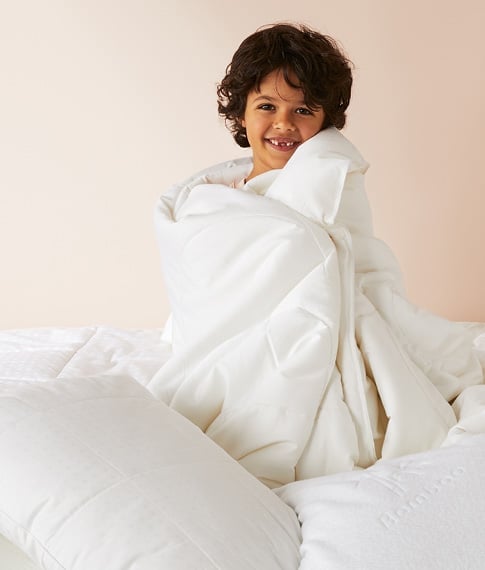 Child sitting up on a bed, cuddling a warm quilt around them, surrounded by pillows. 