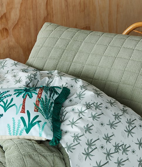 Close-up of quilted kid’s bedlinen with reverse a palm tree print, styled with a matching fringed cushion.