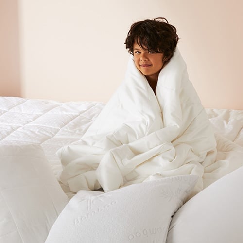 Child sitting on quilt with a selection of pillows, where child is cuddling a quilt around them. 