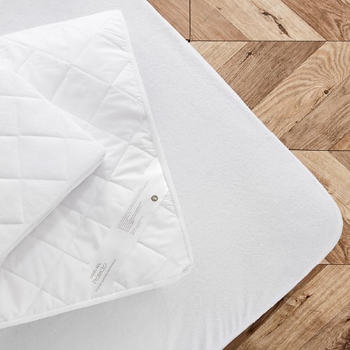 A bird’s eye view of a cot mattress with mattress protector and quilt folded on top.