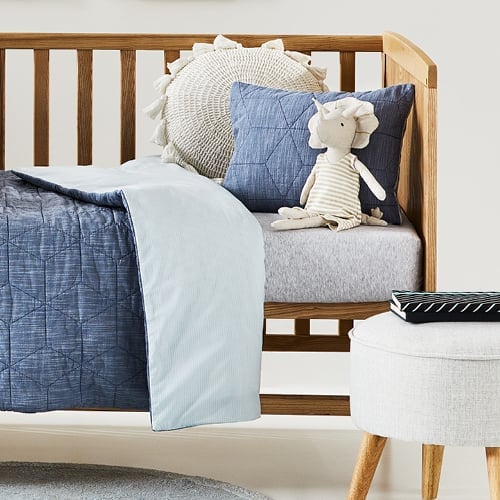 Side-view of cot with grey marle fitted sheet, blue quilted quilt cover, matching pillow (for display only) and unicorn toy.