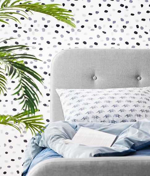 kids grey bed with white dinosaur pattern pillow and light blue sheets. White, grey and blue pattern of wallpaper in the background