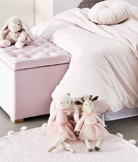 various pink themed plush toys for kids leaning against a pink themed bed with bed sheets, storage chest and pink rug