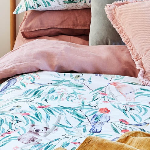Close-up of bedlinen featuring gum leaves and a koala, vintage washed linen pink sheets and warm accessories.
