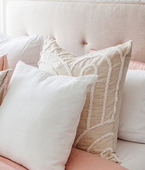 Close-up of two European pillows – one in white and one in a neutral linen colour with white textured detailing. 