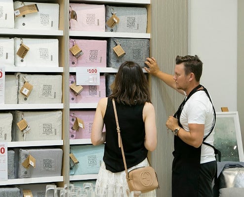 Adairs store setting with staff member helping a customer with a selection of linen sheet sets