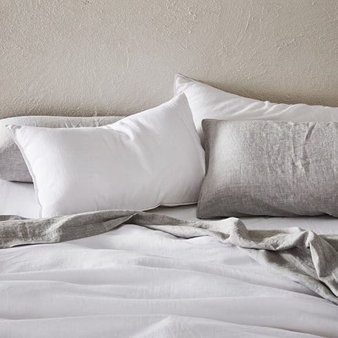 Close-up of bed made with Vintage Washed Linen Quilt Cover in white, grey top sheet and white bottom sheet, plus matching pillows. 