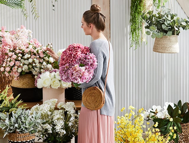 Woman is seen carefully selecting her flowers, she is holding a bouquet of pink toned flowers.
