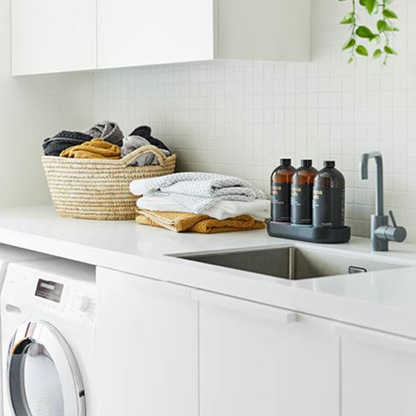 Laundry with white finishes, styled with Navara Bamboo Towels both in a basket and stack, next to a selection of Aroma Wash. 