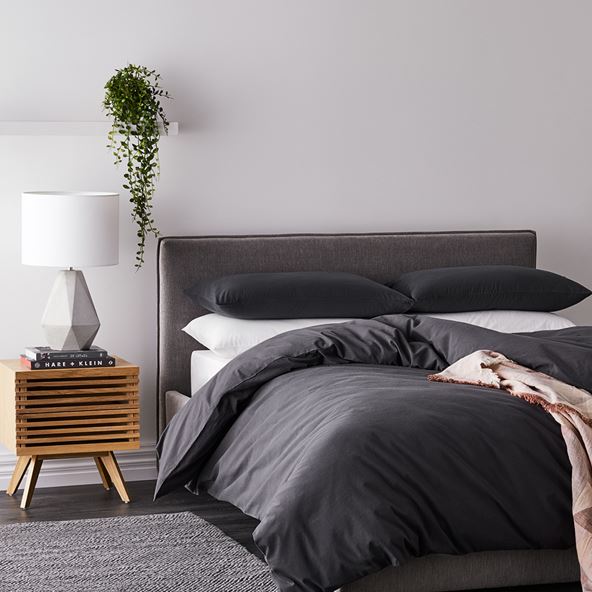 Bed styled with black bedlinen, white sheets, side table and lamp - quilt sits low, bottom edge touching the floor. 