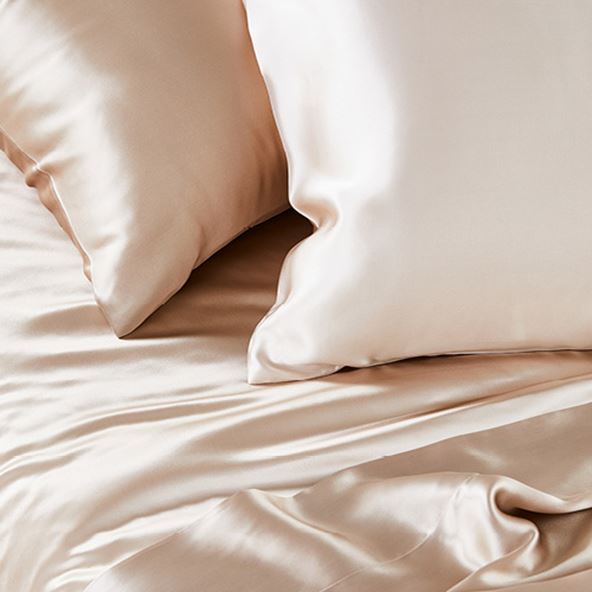 Looking soft to touch, two matching champagne coloured silk pillowcases sit on top of matching silk sheets on a bed.