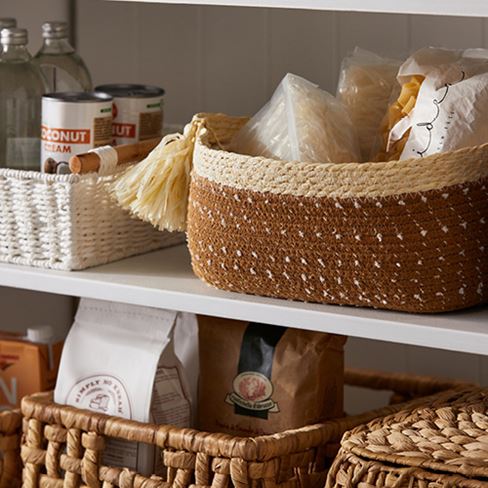 Close up of two shelves of a pantry, white and brown storage baskets with products inside