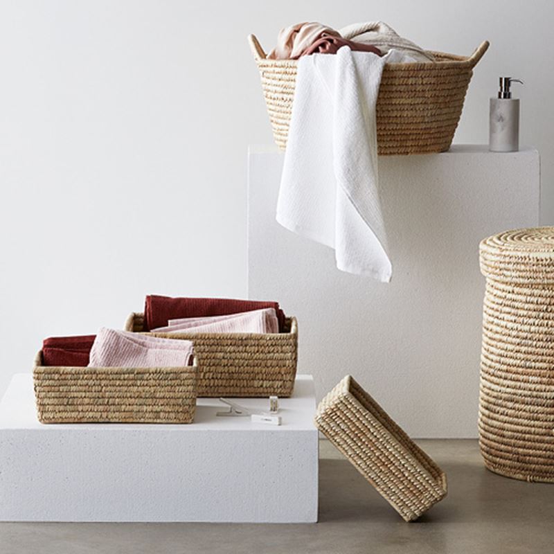 Three brown straw baskets with pink and maroon towels folded inside