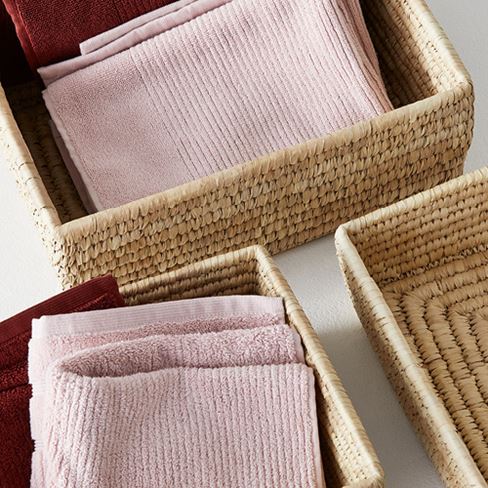 Various light brown straw baskets displayed with pink, white and maroon towels inside