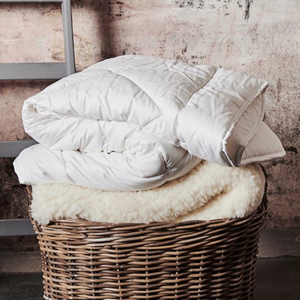 White minijumbuk wool mattress topper folded and placed onto a dark brown bamboo basket