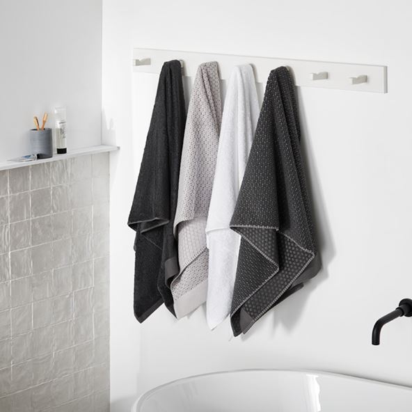 Bathroom with four Flinders Navara Bamboo Towels in charcoal, grey and white above the edge of a bath. 