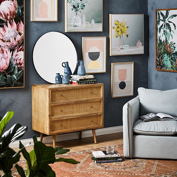 Living room wall styled with multiple artworks at different heights, next to the Arden Natural Chest of 3 Drawers and an Armchair. 