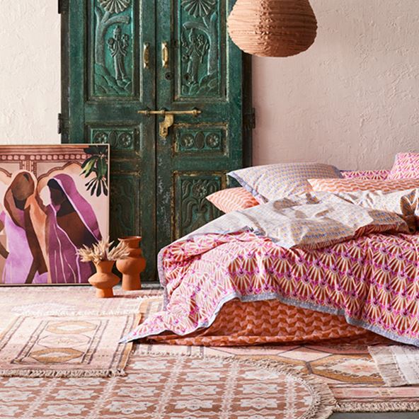 Moroccan inspired bedlinen, bed situated on top of selection of warm tasselled rugs and painting resting against wall next to bed. 