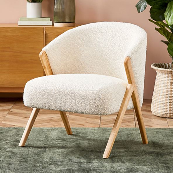 A white armchair in a boucle material sits in the foreground of a room, on an olive rug. 
