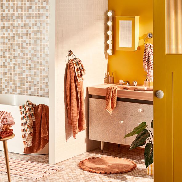 A bathroom scene with a yellow wall, tiled features and towels in shades of terracotta and cream.