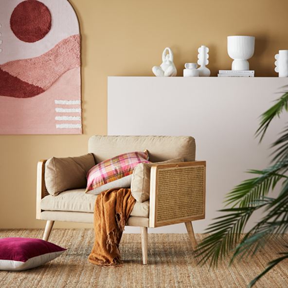 Arna Rattan Chair in neutral styled with pink cushions, and on shelf behind sits a selection of white vases and decor.