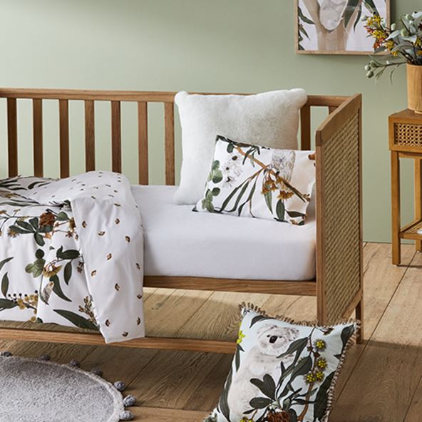 Arden Natural Rattan Nursery Cot with botanical and white matching bedlinen, and a Grey Pom Pom Rug. 