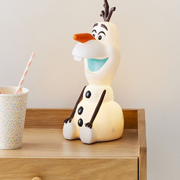 Adairs Kids Disney Frozen II Olaf Night Light turned on siting on a natural wooden bedside table next to a spotty printed cup. 