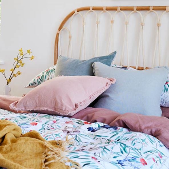 Side-on-view of bed styled with botanical bedlinen and warm hued accessories. 