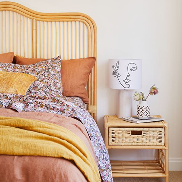 Straight-on image of bed featuring a Rattan Georgia Bedhead, matching side table, lamp and warm-hued bedlinen. 