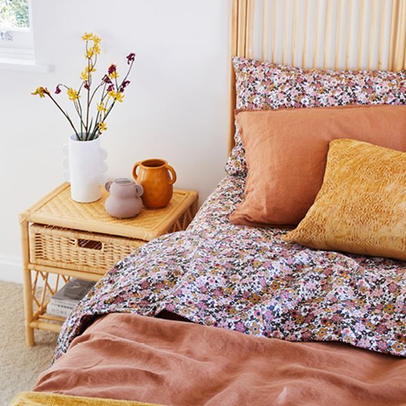 Bed made with floral sheets, Vintage Washed Linen Quilt Cover Set and a Natural Rattan Side Table with a selection of vases. 
