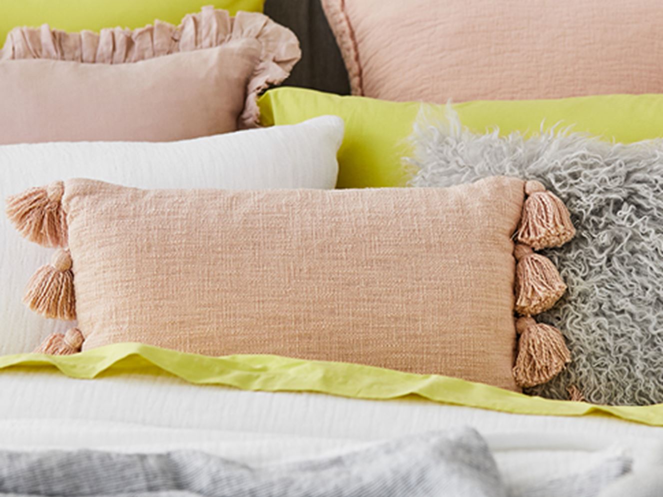 Various pillows with yellow, pink and grey tones placed on the bed